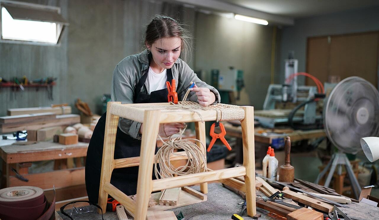 Donna che lavora in grarge per costruire uno sgabello in legno 